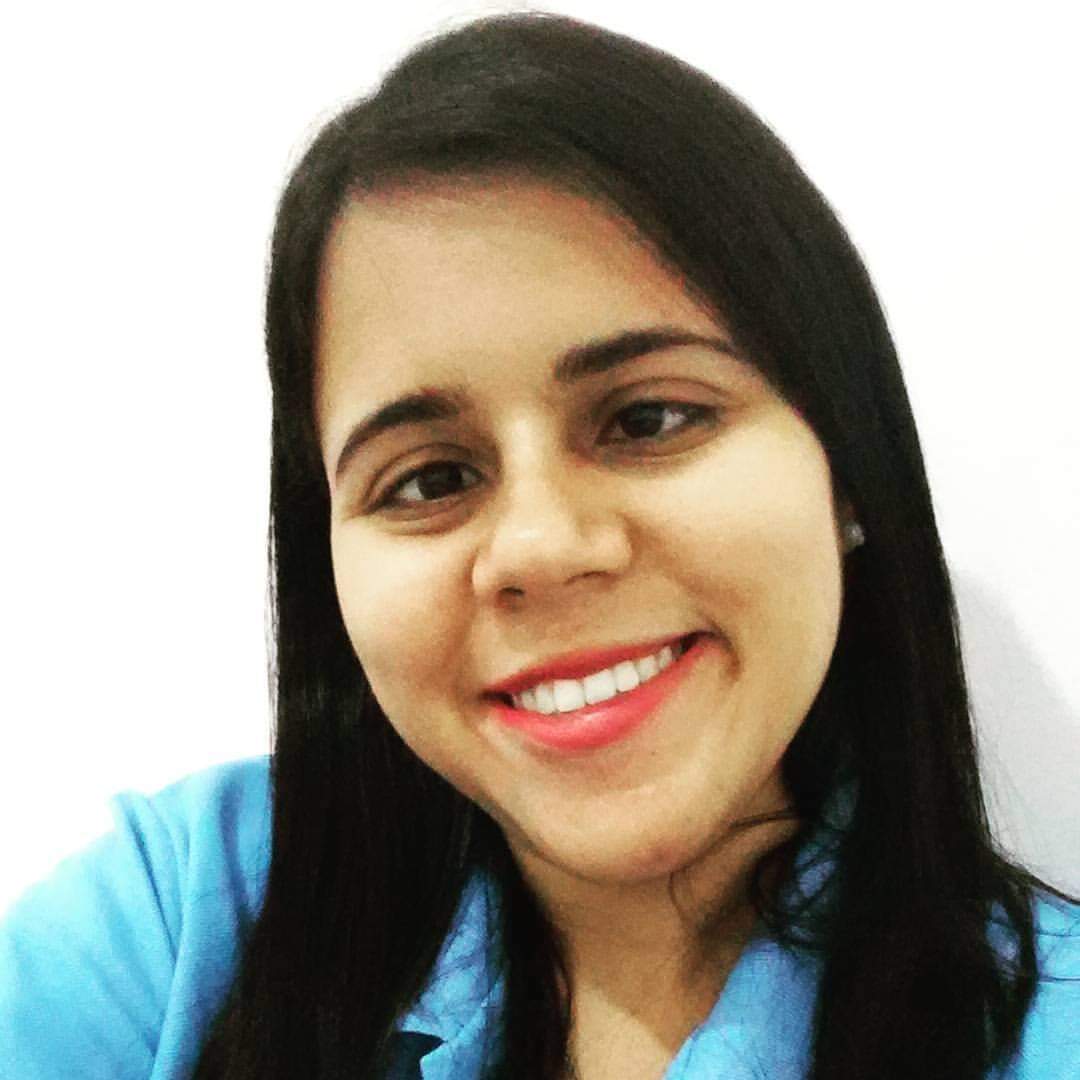 Cassiana é mulher branca com cabelos castanhos escutos na altura dos ombros. Veste blusa azul claro