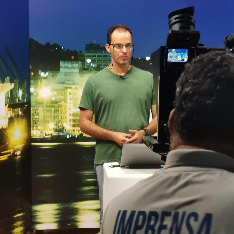 Douglas é homem branco, com cabelos curtos castanhos, óculos ovais. Veste camiseta verde